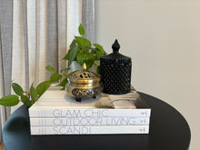 Load image into Gallery viewer, A black 250ml soy wax candle with a geometric design in a cut glass jar, placed on an open book, with a white plant and a decorative vase in the background.