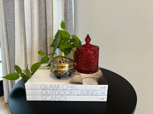 Load image into Gallery viewer, A 250ml soy wax candle in a red glass jar with a geometric design, placed on a black round table with a green plant and a book titled 'Glam Chic Outdoor Living Scandi'.
